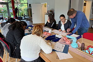 Mehrere Frauen sitzen am Tisch über Büchern und Heften, ein Betreuer beugt sich zu einer Lernenden
